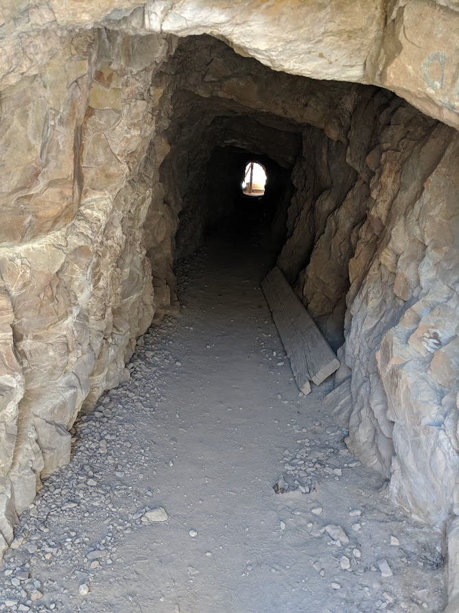 A long tunnel with a low ceiling greets hikers at the top of Perimeter Trail. Hikers crouch to walk to the other end that leads to the Box Canon bridge.